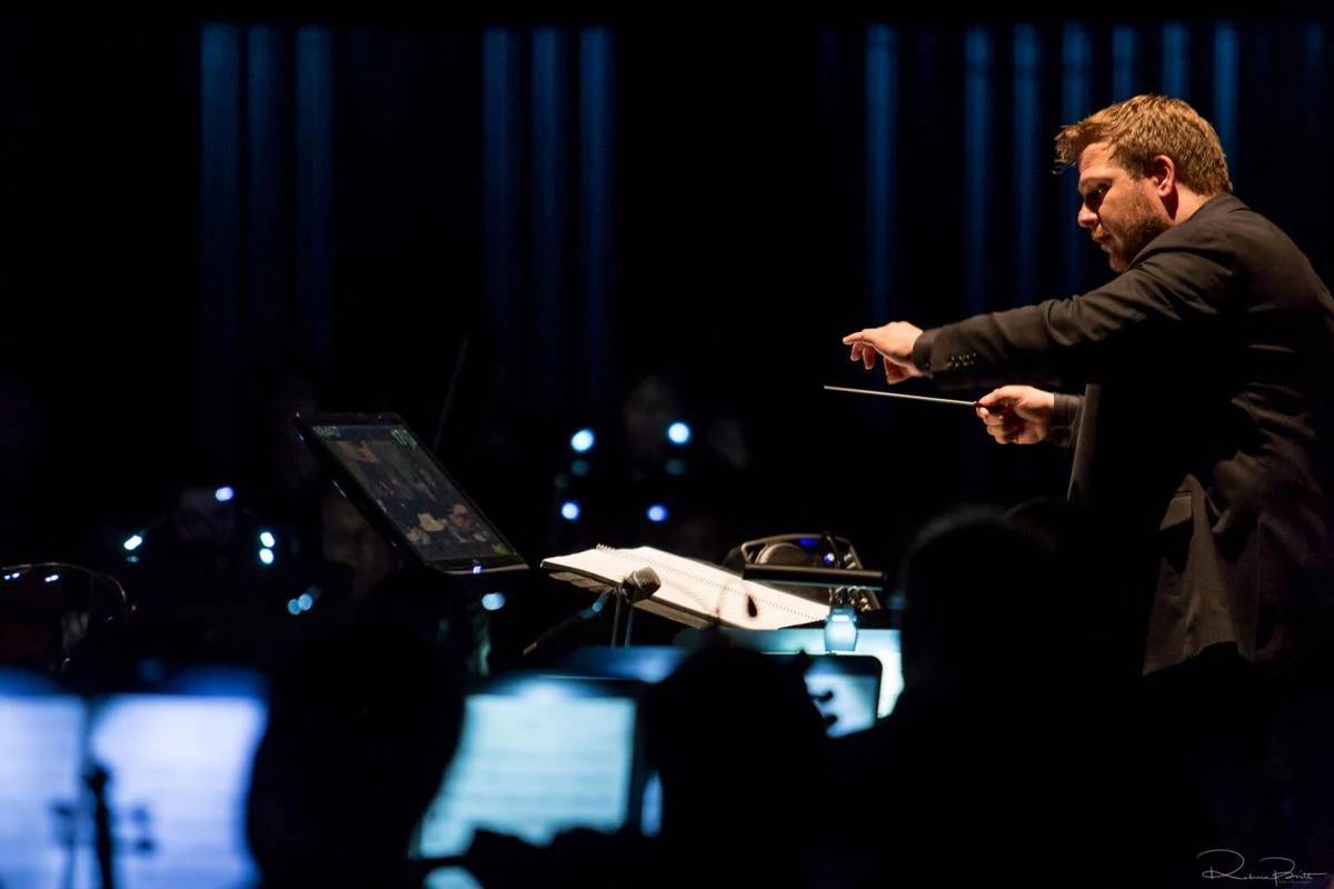 John Jesensky conducting an orchestra on a dimly lit stage, baton in hand
