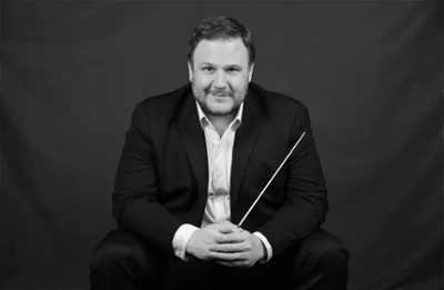 Black and white portrait of John Jesensky seated and holding a conductor's baton